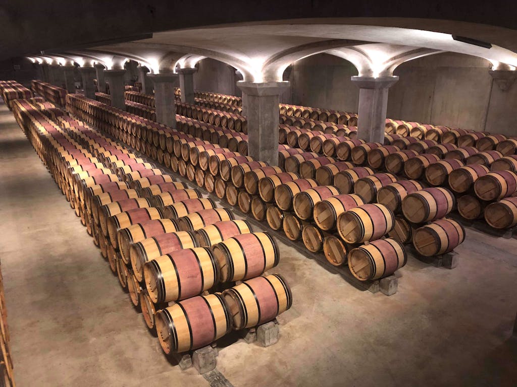 Rows of wooden wine barrels aging in a Margaux winery cellar in France.