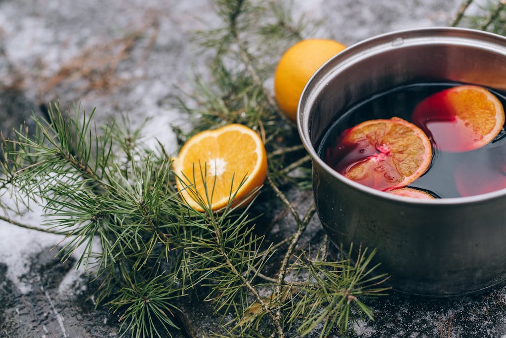 Close-up of mulled wine with oranges in a pot, surrounded by pine branches, perfect for winter holiday themes.