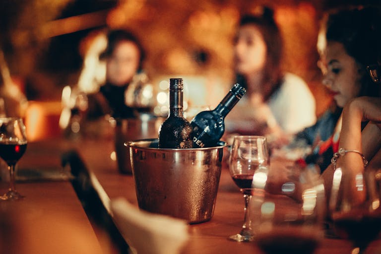 A cozy gathering with wine bottles and glasses on a bar counter, evoking a nightlife atmosphere.